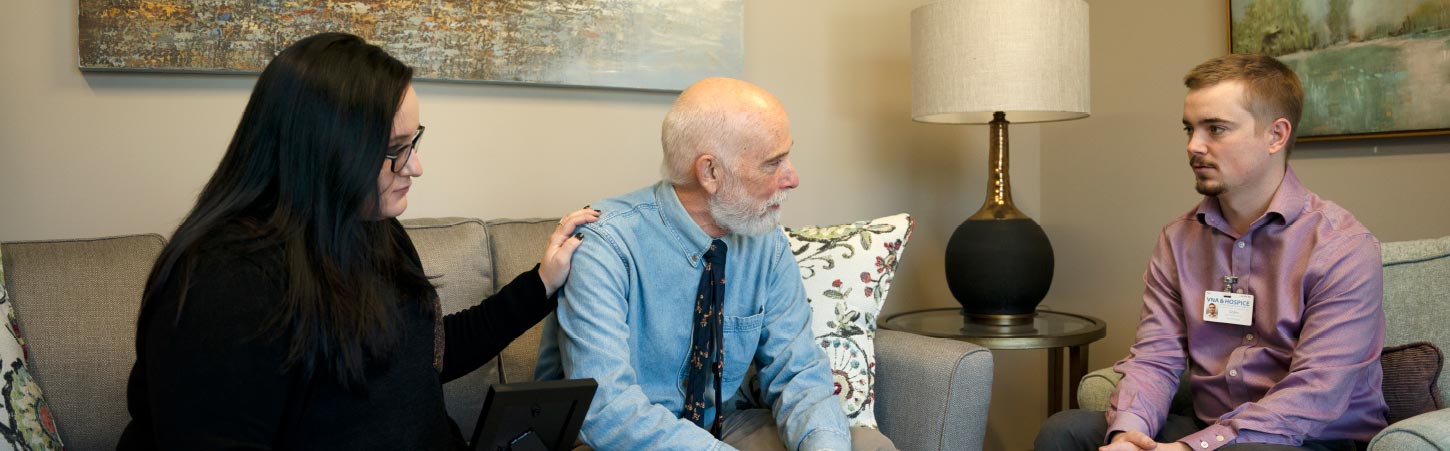 man speaking with a man and woman on couch at hospital