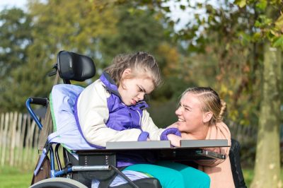 Disability a disabled child in a wheelchair relaxing outside together with a care assistant