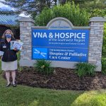 woman holding books and pajamas at VNA & Hospice sign on property